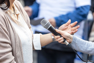 Journalist holding microphone making media interview with female politician or business woman