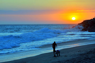 People on beach against sky during sunset