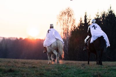 Rear view of men riding horses on field against sky