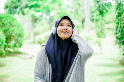 Beautiful young asian muslim woman listening to music with headphones in a park