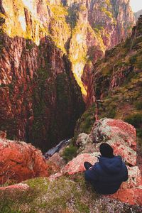 Rear view of man sitting on rock formation