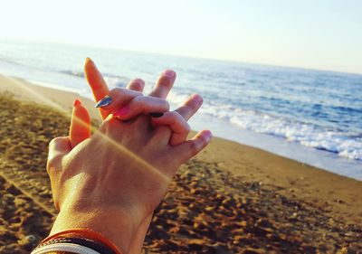 Close-up of woman hand on sand at beach against sky