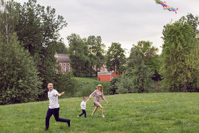 Family mom, dad and son launches an aerial flying kite on a field in the summer