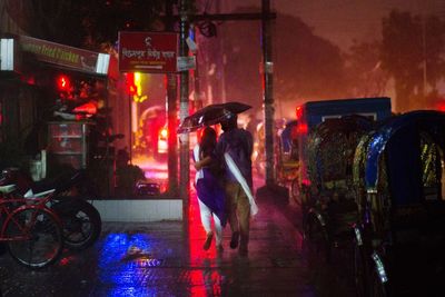 Woman on wet street in illuminated city during rainy season at night
