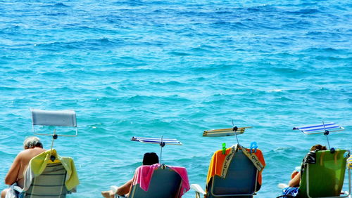 Rear view of people relaxing on lounge chairs at beach