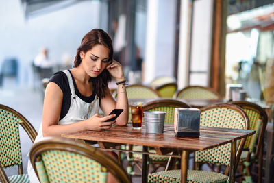 Young woman using phone while sitting at outdoor cafe