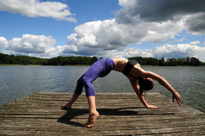 Full length of young woman doing yoga on jetty by lake