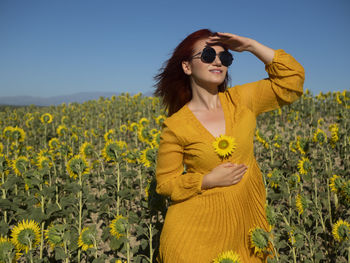 Portrait of young woman standing against yellow flowers
