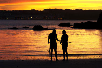 Silhouette men on beach against sky at sunset