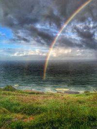 Rainbow over sea against cloudy sky