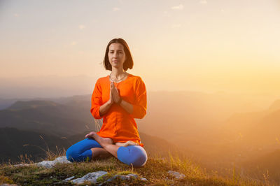 Yogi woman sits in a lotus position with crossed legs and holds her hands to her chest against the