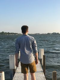 Rear view of man standing on sea against clear sky
