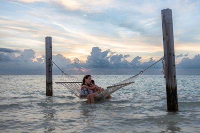 Rear view of woman sitting on boat in sea against sky during sunset