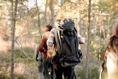 Rear view of man walking with friends while hiking in forest