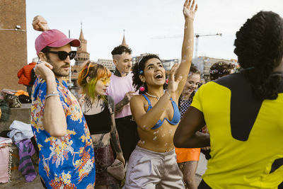 Happy non-binary friends dancing amidst bubbles in city