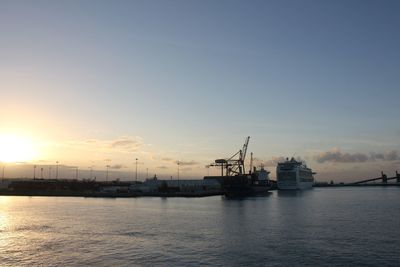 Silhouette cranes at harbor against sky during sunset