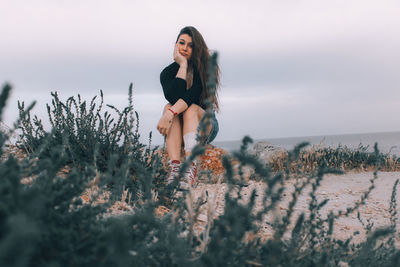 Young woman sitting on plant against sky