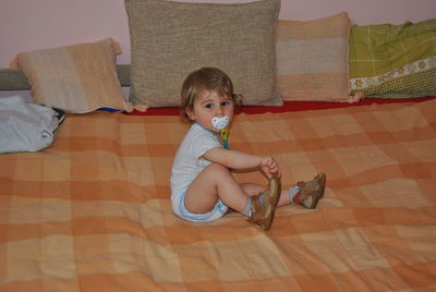 Portrait of cute baby boy sucking pacifier on bed at home