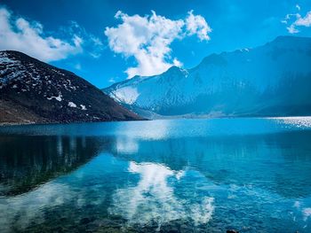 Scenic view of lake by snowcapped mountains against blue sky