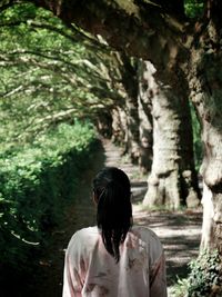 Rear view of woman walking against trees at park