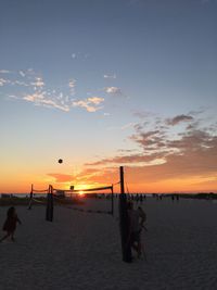 Silhouette people on beach against sky during sunset