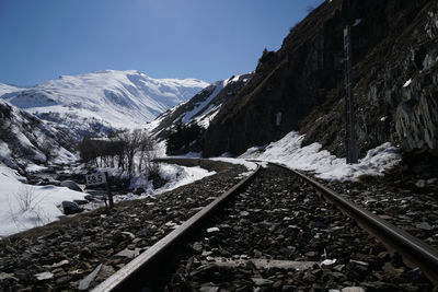 Railroad tracks amidst snowcapped mountains against clear sky