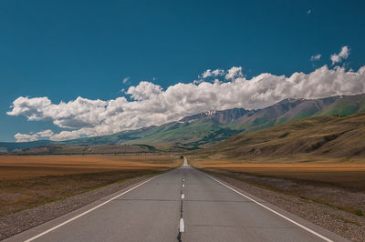 Empty road leading towards mountains against cloudy sky