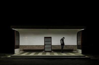 Side view of young man with backpack standing at bus stop