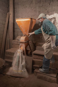 Full body side view of male worker in uniform and respirator standing near industrial plaster station in professional ceramic workshop