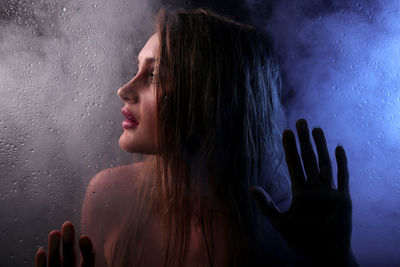 Portrait of woman looking through wet glass