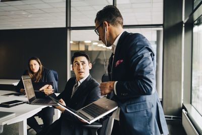 Male professionals discussing over laptop in conference room at office