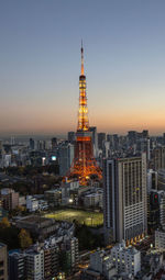 Illuminated tokyo tower in city against clear sky during sunset