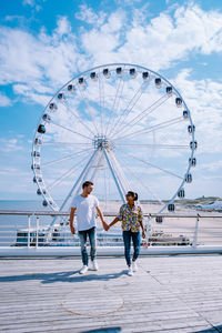 People standing in amusement park by sea against sky