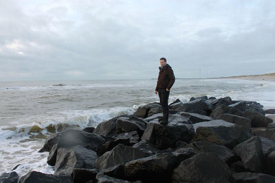 Thoughtful man standing on rocky shore against cloudy sky during sunset