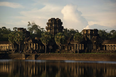 Built structure and trees by lake against sky