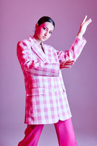 Portrait of young woman standing against gray background