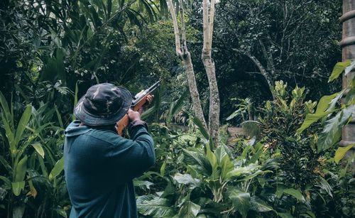 Rear view of man shooting with rifle against trees