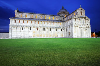 Pisa cathedral by lawn against blue sky at dusk