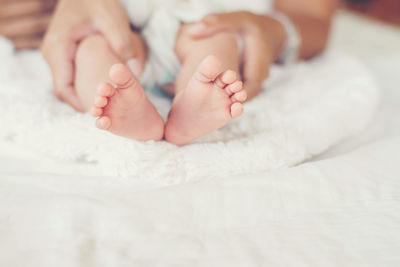 Cropped hands of mother holding baby feet on bed