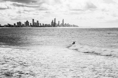 Scenic view of sea and buildings against sky and a surfer