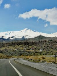 Road by snowcapped mountains against sky