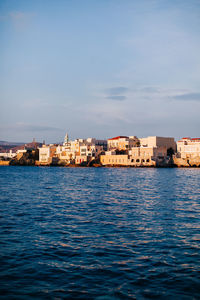 Sea by buildings in city against sky