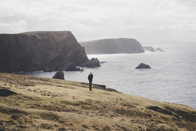 Mid distance view of person standing on cliff against sea