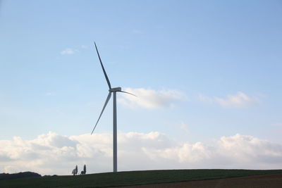 Low angle view of windmills on field against sky