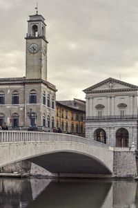 Arch bridge over river by buildings against sky