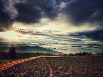 Scenic view of field against cloudy sky on sunny day