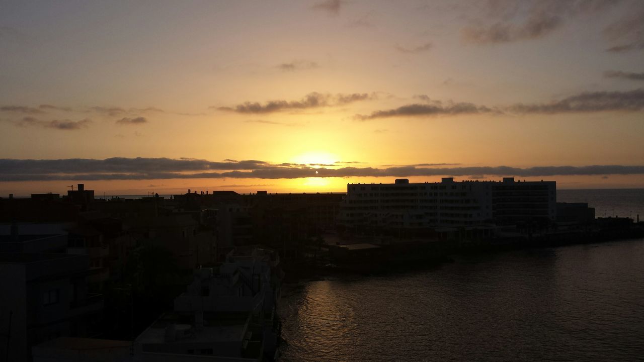 sunset, building exterior, architecture, built structure, water, sea, sky, orange color, silhouette, city, sun, cloud - sky, horizon over water, cityscape, scenics, beauty in nature, sunlight, nature, outdoors, residential building