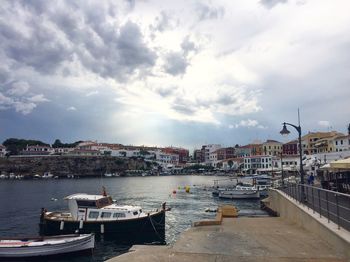 Boats moored in river by buildings against sky