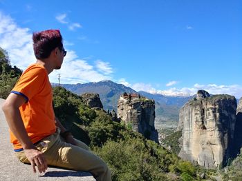 Side view of man sitting on mountain against sky