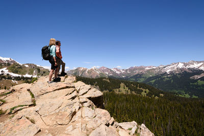 Man and woman standing on rock against mountains and blue sky